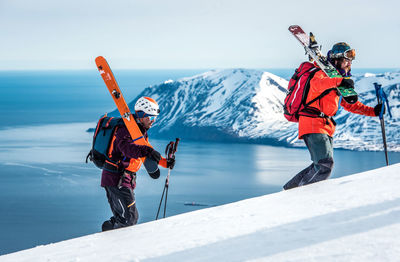 Men hiking uphill with skis and ocean and mountain behind them