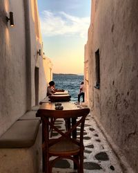 Man and woman in alley by sea against sky during sunset