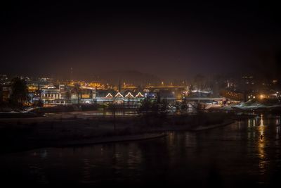 Illuminated cityscape by river against sky at night