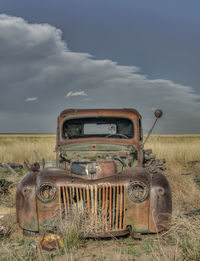 Abandoned car on field against sky