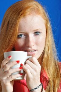 Close-up portrait of teenage girl holding coffee cup against wall