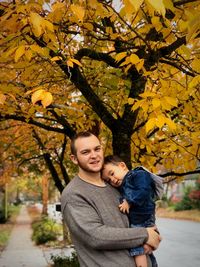 Portrait of father carrying son against autumn trees
