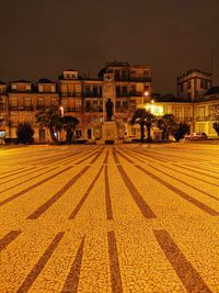 Illuminated street by buildings against sky at night