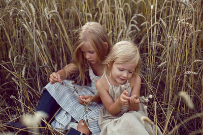 Two blonde sisters sit in a field among dry wheat in the summer