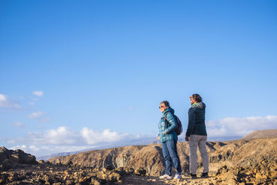 Hikers standing on landscape against blue sky