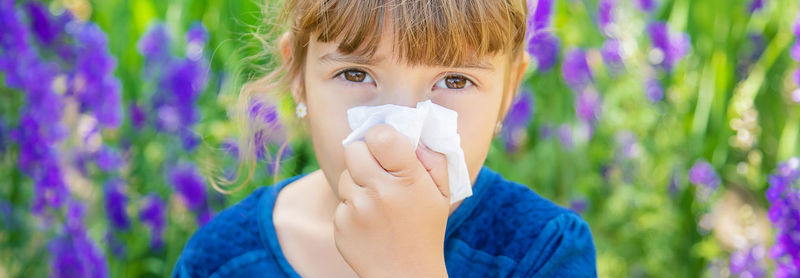 Portrait of girl wiping nose against plants