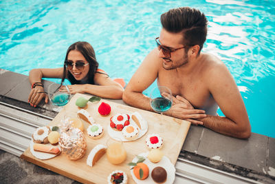 Beautiful couple enjoying tasty food in pool during tropical vacation