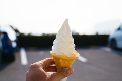 Close-up of hand holding ice cream cone against sky