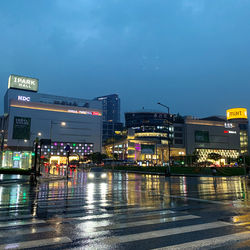 Illuminated city by buildings against sky during rainy season