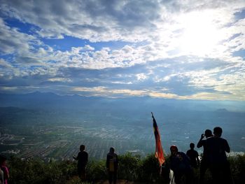 Rear view of people walking on landscape against cloudy sky
