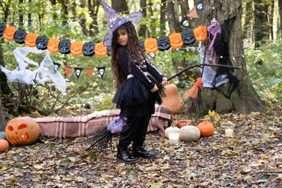 Arab girl in halloween costume and witch hat with broom in halloween decoration outdoor