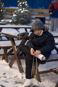 Full length of boy wearing ice skate while sitting on bench