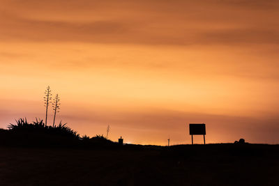 Scenic view of the silhouette of a field and a traffic sign against sky during sunset