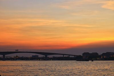 Silhouette bridge over river against romantic sky at sunset