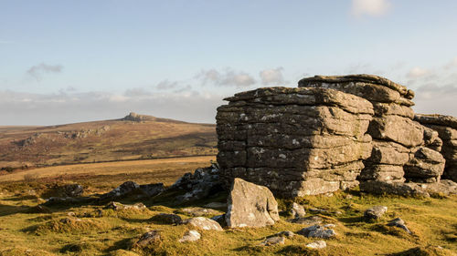 Stone wall on rock formation on field against sky