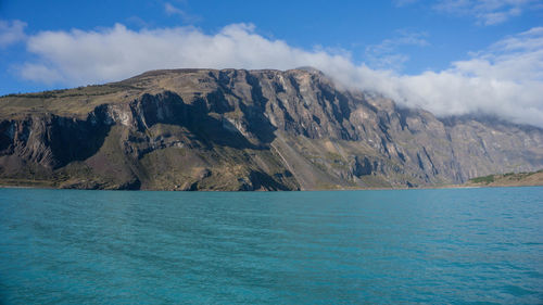 Scenic view of sea by mountain against sky