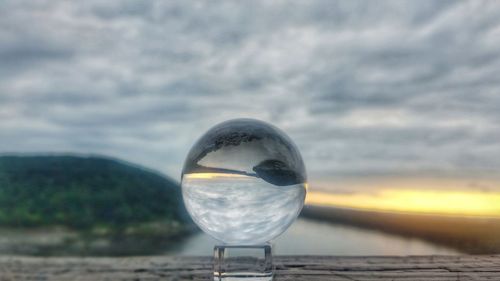 Close-up of crystal ball on sea shore against sky