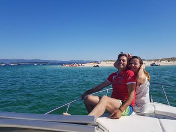 Portrait of smiling couple sitting on boat in sea against clear blue sky