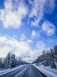 Empty road by trees against blue sky