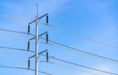 Low angle view of electricity pylon against clear blue sky