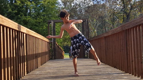 Full length of boy throwing stone at wooden footbridge