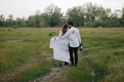 Newlywed couple walking on field against sky