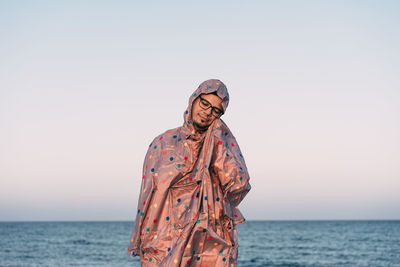 Person standing in raincoat by sea against clear sky