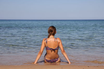 Rear view of woman in bikini standing at beach against clear sky
