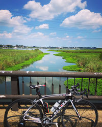 Bicycle by railing on field against sky