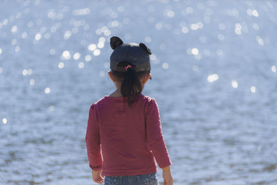 Rear view of girl standing against sea at beach