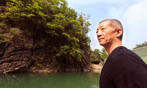 Thoughtful mature man looking away while standing at lakeshore against sky