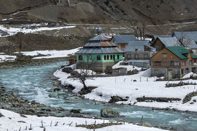 Snow covered houses by lake against buildings