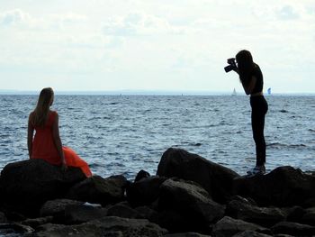 Rear view of people photographing sea against sky