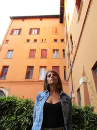 Low angle view of young woman looking away against building