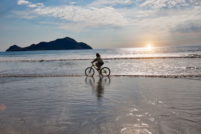 Man cycling on beach during sunset