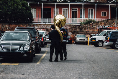 Rear view of man with friend carrying brass instrument in parking lot