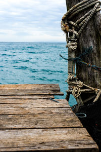 Rope tied to wooden post in sea against sky