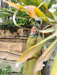 Portrait of smiling young woman standing against plants