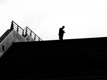 Low angle view of silhouette man standing on staircase against clear sky