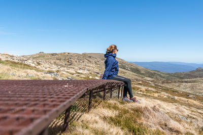 Woman sitting on mountain against blue sky