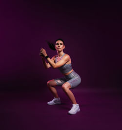 Full length of young woman exercising against black background