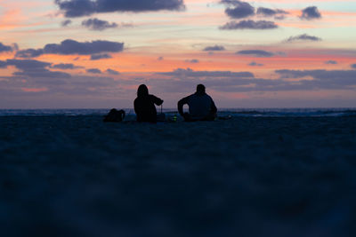 People sitting on beach against sky during sunset