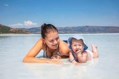 Mother lying down on beach with daughter against sky