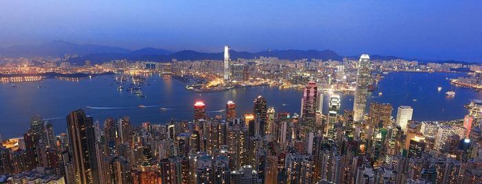 Panoramic view of illuminated cityscape by river against sky
