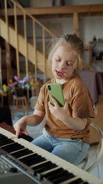Girl using mobile phone while playing piano