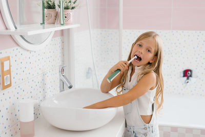 Cute child girl brushing her teeth in front of the bathroom mirror in the morning