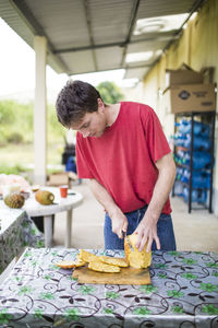 Young man cutting fresh, organic pineapple on wood cutting board.