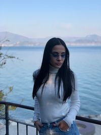 Beautiful woman standing by railing against sea 