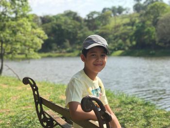 Portrait of smiling boy sitting on bench by river