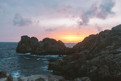 Rocks on shore against sky during sunset